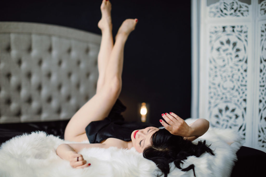 An example of what to wear to a boudoir photo session - a photo of a nude woman laying in bed partially covered with a black sheet.