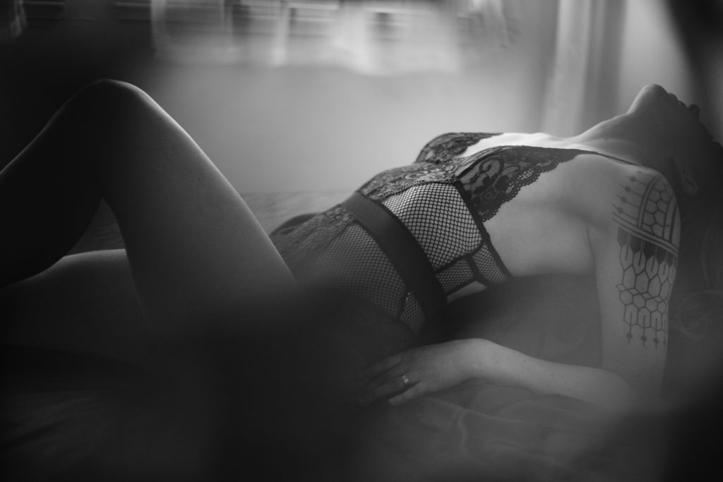 An example of what to wear for a boudoir photo shoot - a photo of a woman in black lingerie, partially obscured, while she is leaning back in a bed.