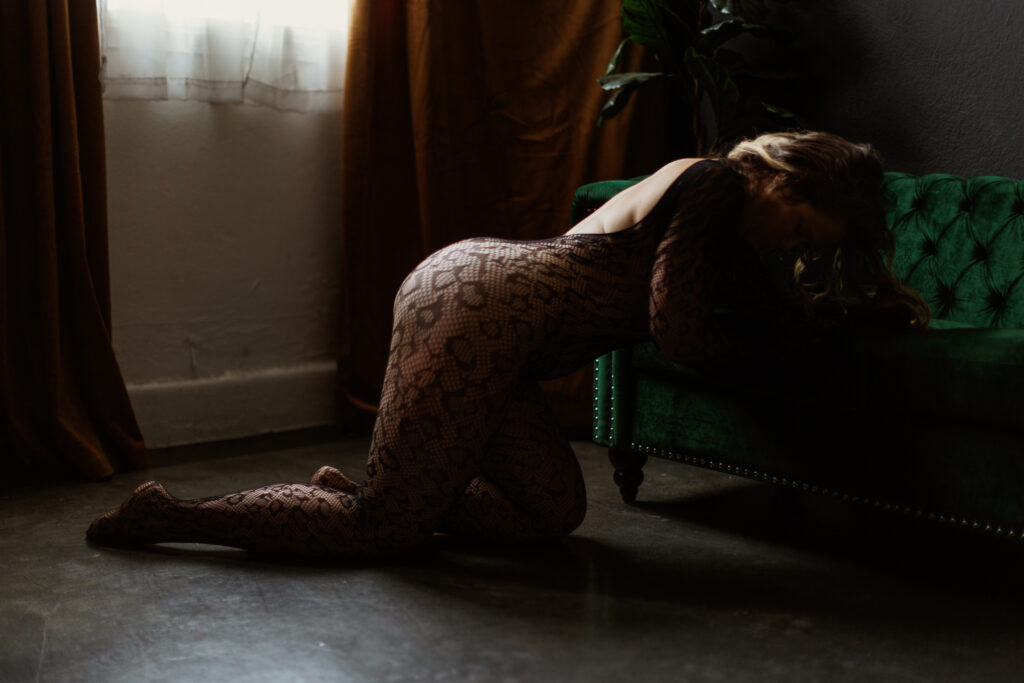 San Jose Boudoir Photographer leaning on green velvet couch, wearing black mesh body suit. 