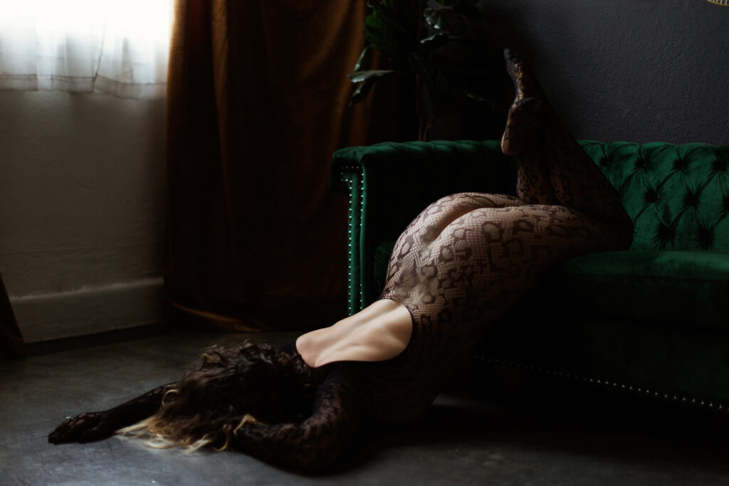 Woman in black mesh lingerie laying partially on green couch and partially on the ground.