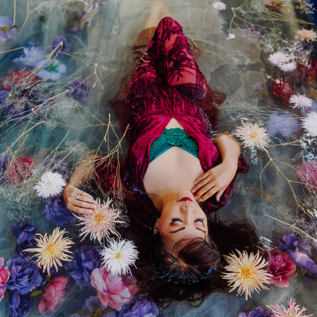 Woman in red robe and green bra in a bath of pink and purple flowers